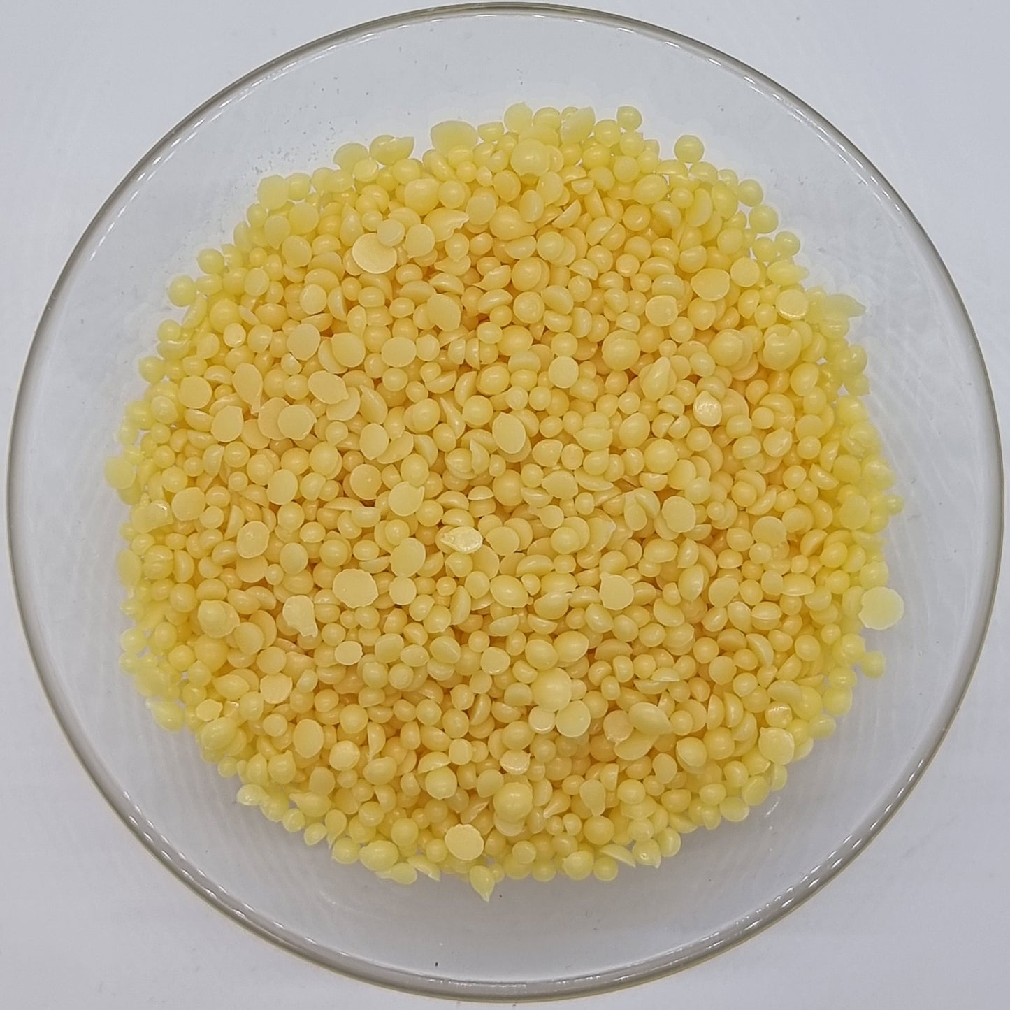 glass bowl containing lots of irregular round shaped with flat back pellets of Candelilla wax, a vegetable substitute for beeswax, suitable for vegans and widely used in soap and cosmetic making recipes.