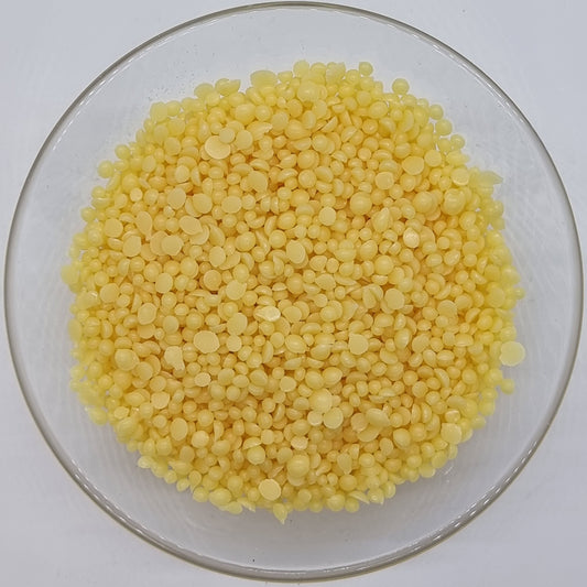 glass bowl containing lots of irregular round shaped with flat back pellets of Candelilla wax, a vegetable substitute for beeswax, suitable for vegans and widely used in soap and cosmetic making recipes.