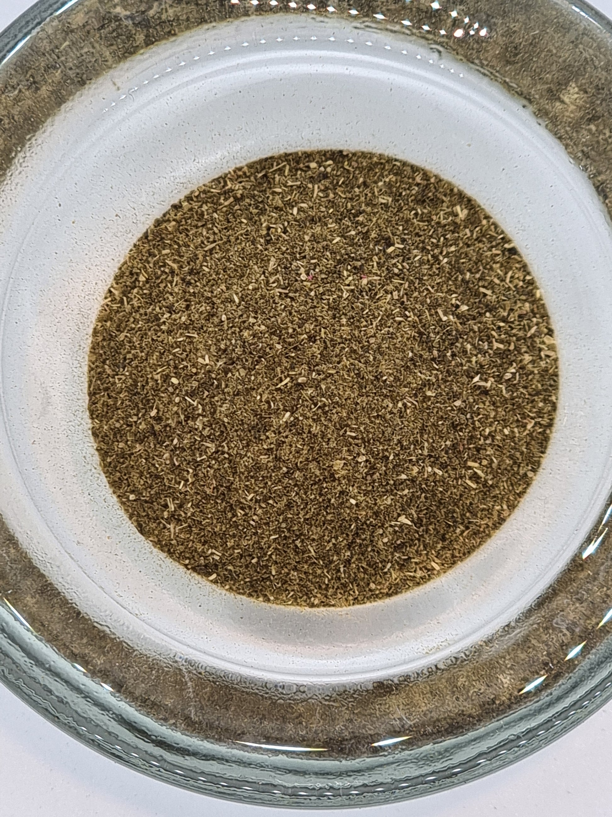 a glass bowl filled with dried very finely chopped green tea leaves that are almost powder form The colour is a muted deep green with lighter flecks.