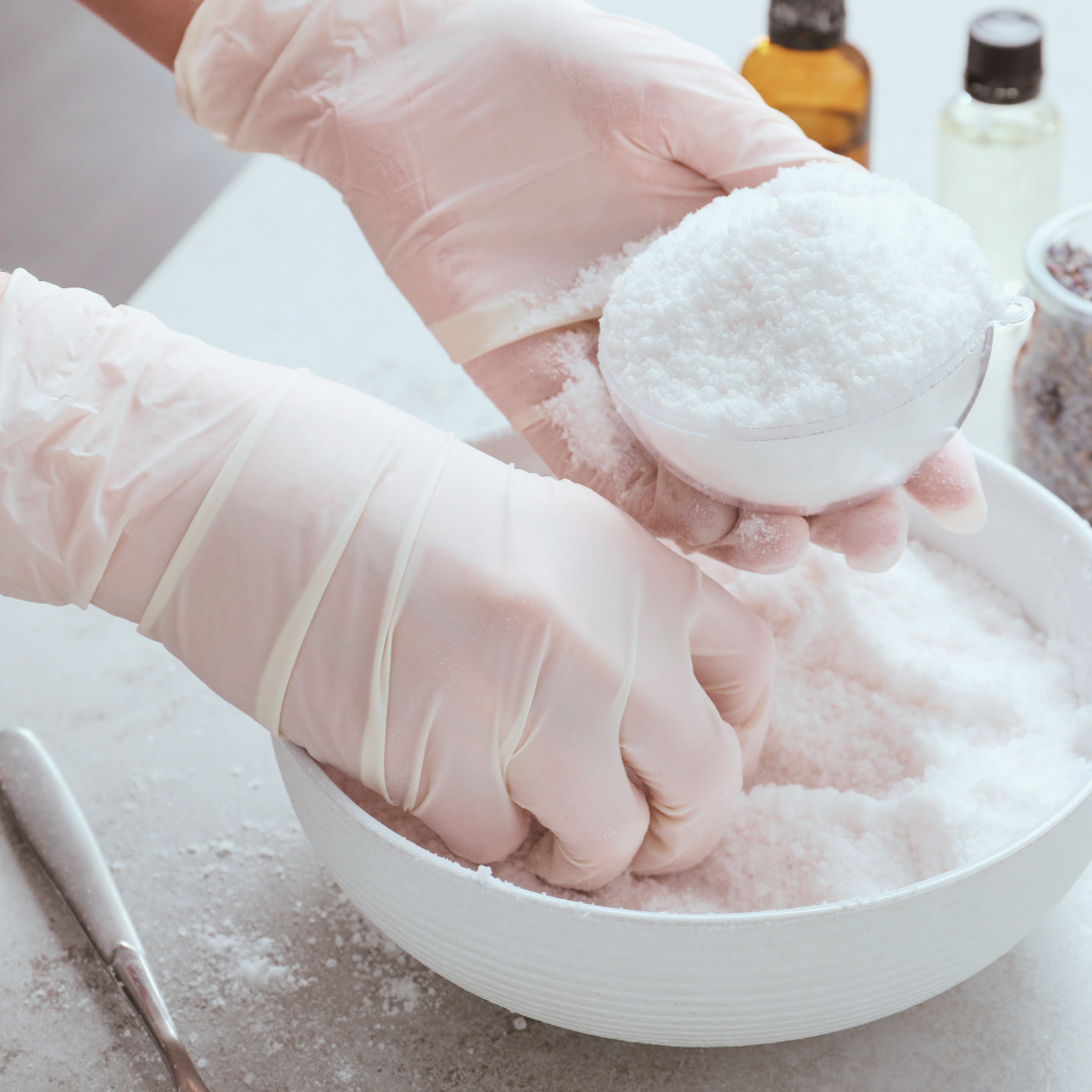 Gloved hands in a bowl with white dry ingredients and a bath bomb mould