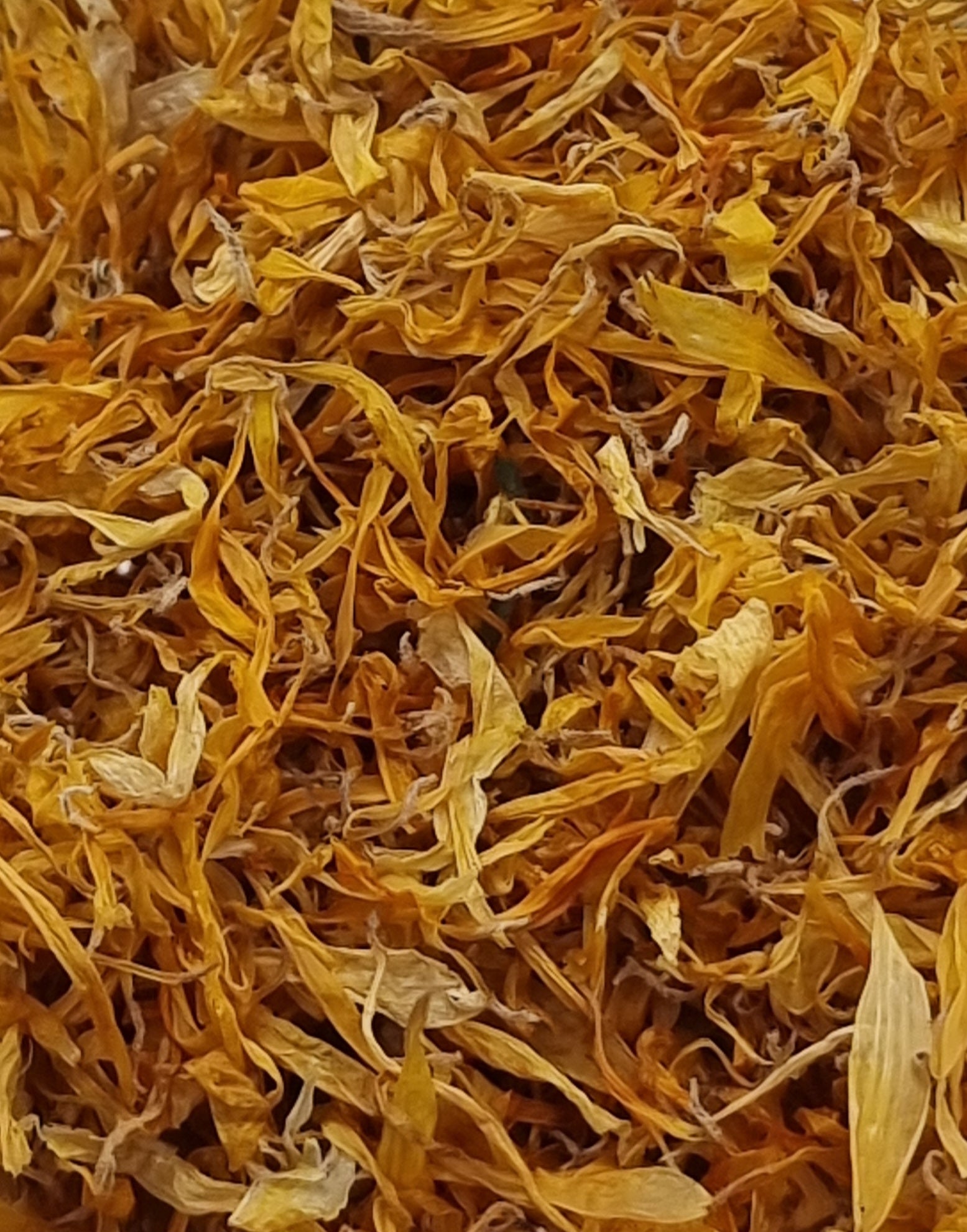 close up photo of dried calendula petals showing the variety of yellow to orange colours. The petals are small, similar sizes and variations of elongated oval shapes with slight curls at the edges