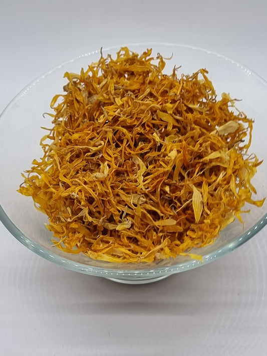 a glass bowl filled with small yellow calendula flower petals that are dried and range from deep orange yellow to light bright yellow. Each petal is an elongated oval shape and varies in its exact shape