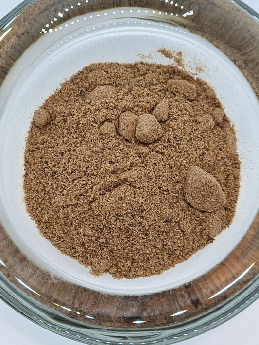 a glass bowl containing finely ground dried nutmeg powder which is a mid brown to orange colour.