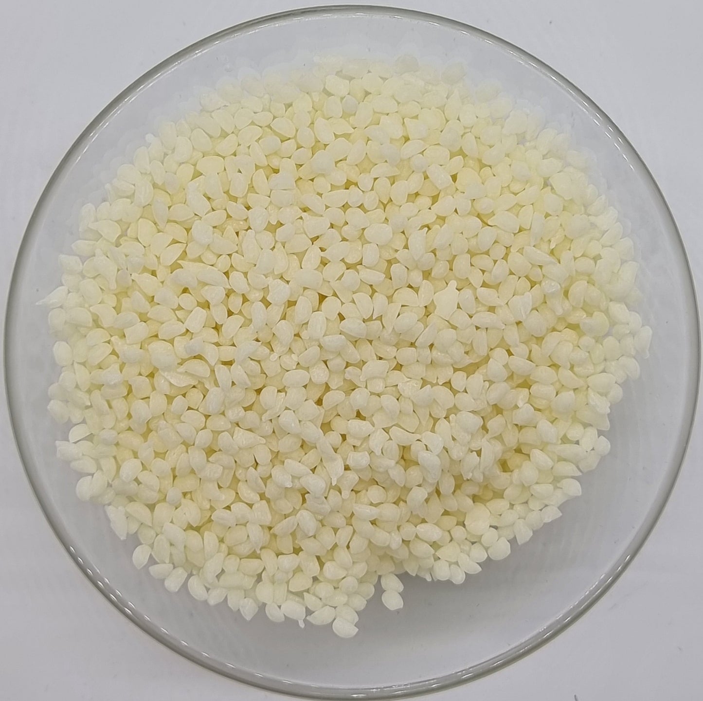 glass bowl containing lots of small irregular oval shaped pellets of refined white beeswax for soap and cosmetic recipes