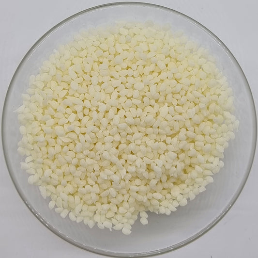 glass bowl containing lots of small irregular oval shaped pellets of refined white beeswax for soap and cosmetic recipes
